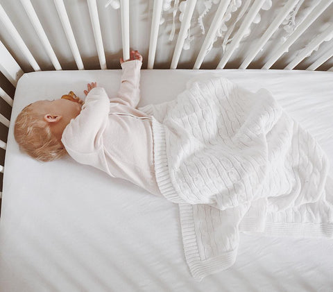 Baby sleeping on side in crib with white surroundings