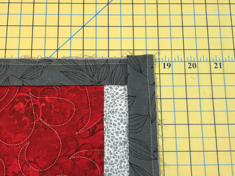Red and gray patchwork quilt with gray binding sewn on and mitered at the corner.