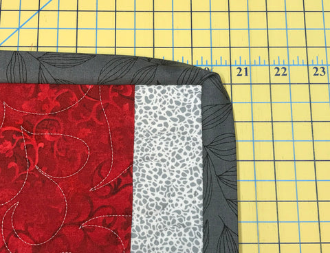 Mitered corner of quilt binding on red and white patchwork quilt.