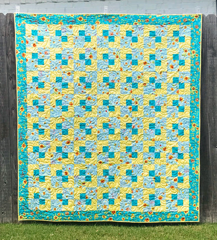 Teal and yellow patchwork quilt shown hanging on a fence.