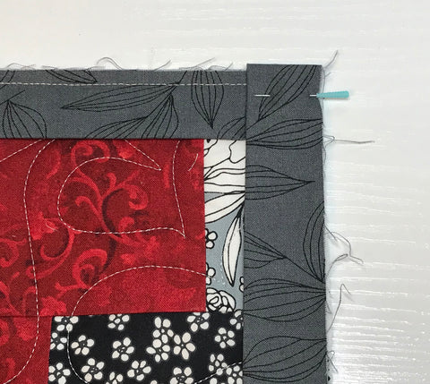 Red and gray patchwork quilt with gray binding being attached, showing the binding strip folded down and pinned for mitered corner.