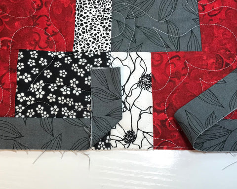 Red and gray patchwork quilt with two gray binding ends laying across it.