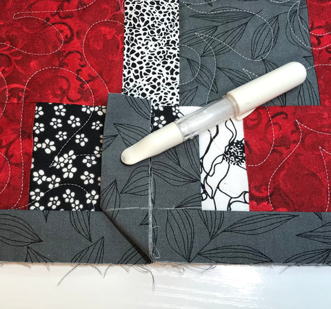 Red and gray patchwork quilt with two gray binding ends laying across it. Binding ends are both folded up at 90 degree angle and marked with white chalk along horizontal binding line.