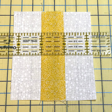 Three strips of fabric sewn together to test the accuracy of a quarter inch seam for quilt piecing.