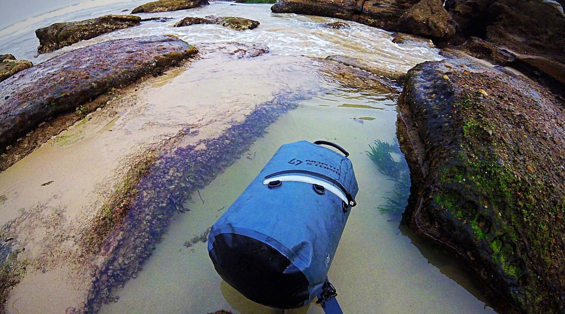 A NORTH STORM 20 LITRE DRY BAG FLOATING IN A ROCK POOL AT THE BEACH.