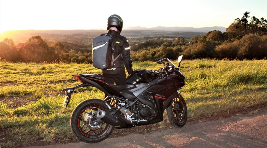 A MAN STANDING BY HIS MOTORBIKE WEARING A NORTH STORM WATERPROOF BACKPACK.