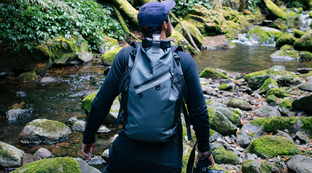 A man in the bush standing by a creek wearing a North Storm 30 litre waterproof backpack. 