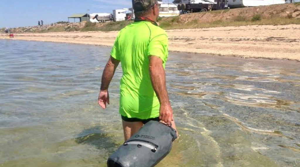 A MAN WADING THROUGH THE WATER TOWING HIS NORTH STORM WATERPROOF DRY BAG.