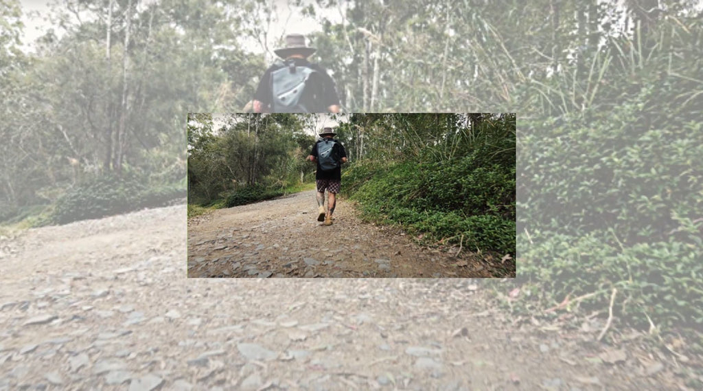 A man wearing a wide brimmed hat walking up a bush track wearing his 30 Litre North Storm waterproof backpack. 