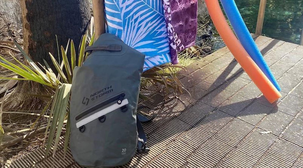 A North Storm 20L Dry bag leaning against a pole with a towel and a pool noodle next to it. Ready go and have some fun swimming. 