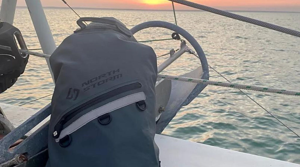 A North Storm® 20 litre dry bag on deck of a boat with the sun setting over the ocean in the background, creating a romantic scene. 