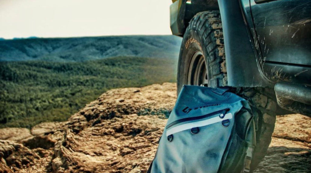 A 4 wheel drive with a North Storm® 30L Waterproof Backpack rested against a tyre. 
