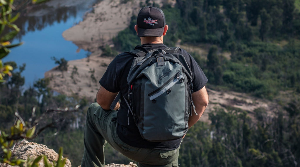 Man standing with his leg up on a rock looking out over the cliff at spectacular views. He is also wearing his North Storm® 30L Waterproof Backpack. 