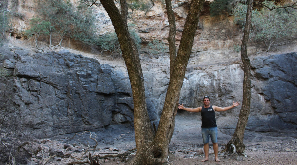 A MAN STANDING IN A VERY DRY BUSH SURROUNDED BY HUGE SHEER ROCKY CLIFF FACES.