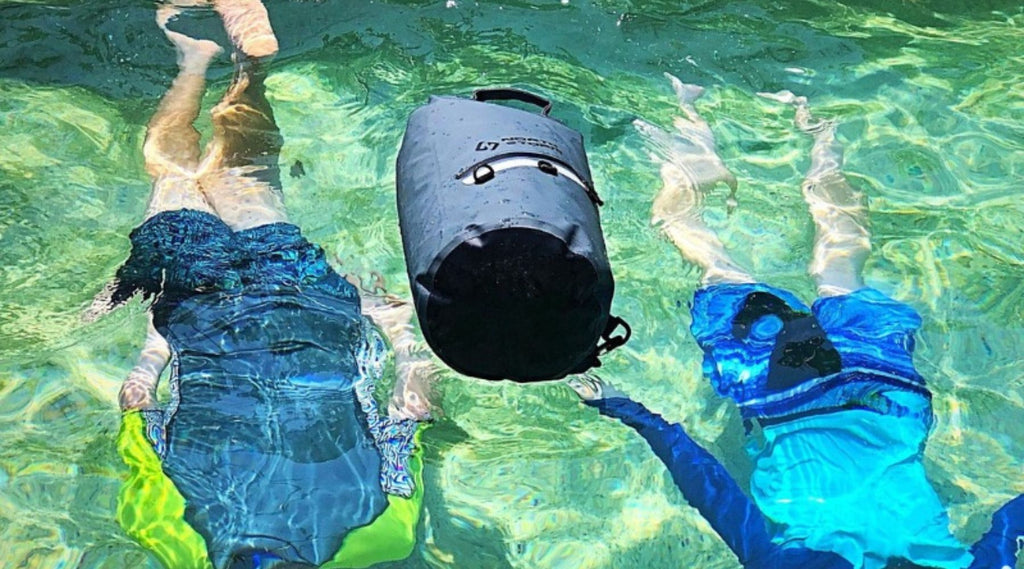 TWO CHILDREN SWIMMING UNDERNEATH A 20 LITRE NORTH STORM DRY BAG IN A SWIMMING POOL. THE DRY BAG IS FLOATING ON THE WATER ABOVE THEM. 