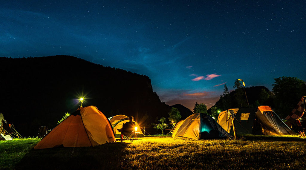 A GROUP OF TENTS AT A CAMPSITE AT NIGHT WITH LIGHTS SHINING.