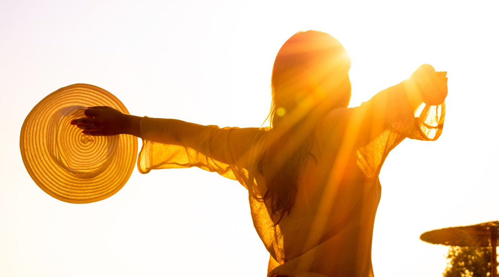 A LADY WITH HER ARMS OUTSTRETCHED WITH THE SUN BEAMING DOWN ON HER.