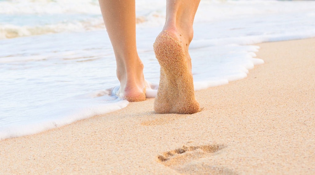A PERSONS FEET WALKING THROUGH THE SHALLOWS OF THE WAVES MAKING FOOTPRINTS IN THE SAND.