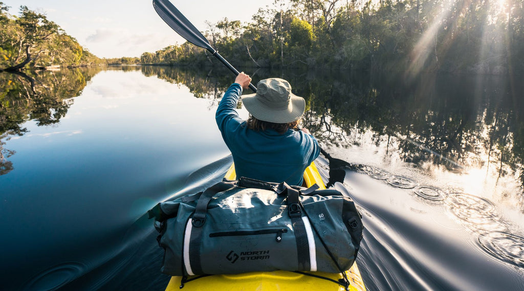 Man paddling up a calm river with a North Storm waterproof duffel bag