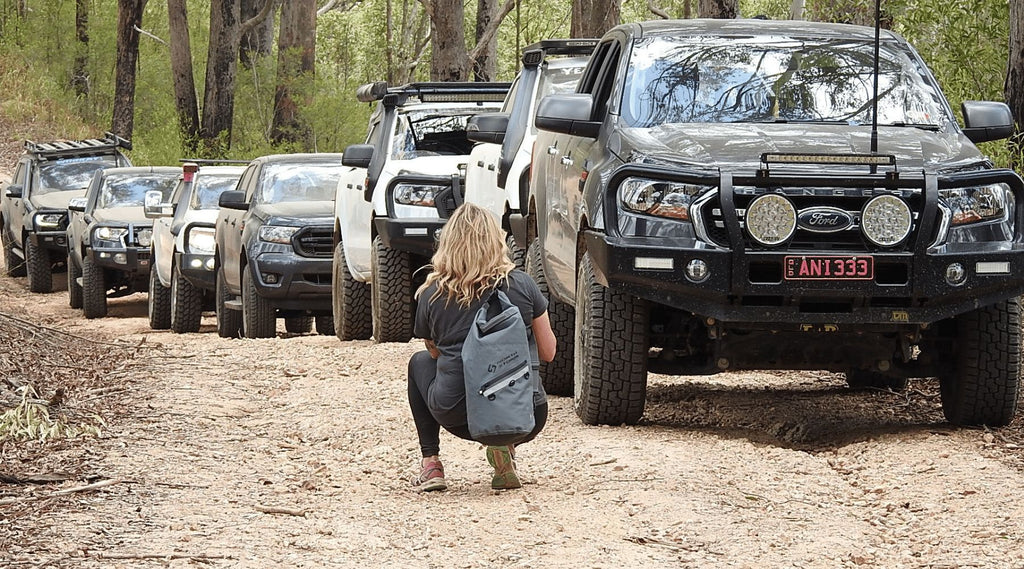 A LINE UP OF FORD RANGERS WITH FOUNDER JANE CARTWRIGHT CROUCHED IN FRONT TAKING A PHOTO WEARING A NORTH STORM 20 LITRE DRY BAG.