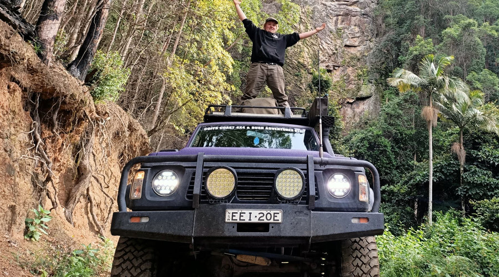 TOMMO STANDING ON THE ROOF OF HIS 4X4 WITH HIS ARMS OUTSTRETCHED.