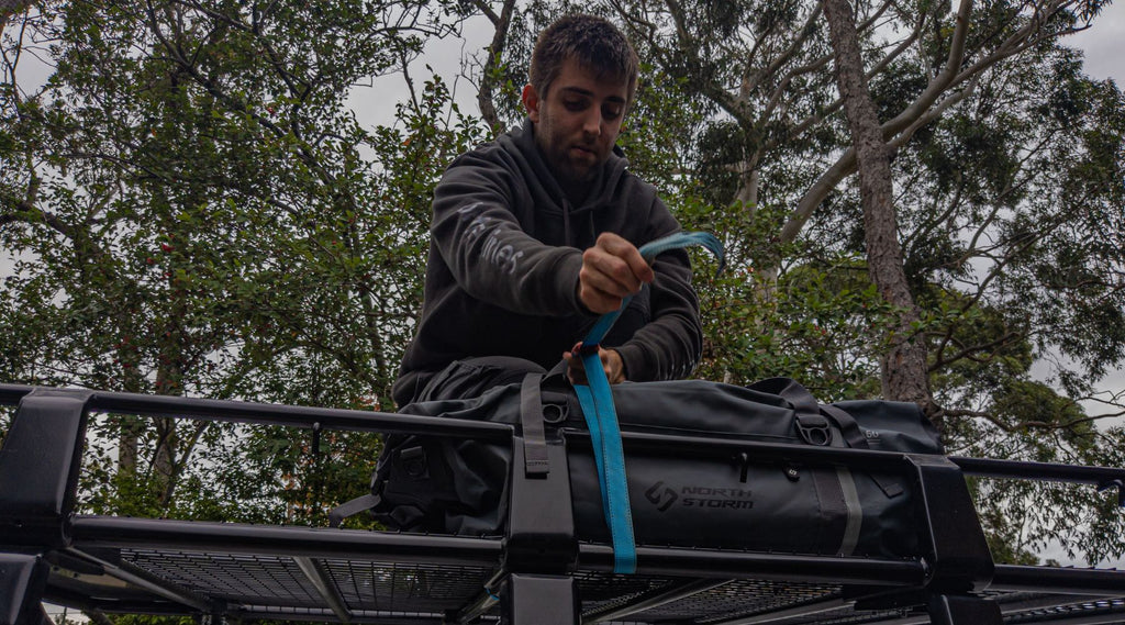 MAN TIEING A NORTH STORM DUFFEL BAG TO THE ROOF RACKS OF HIS 4 WHEEL DRIVE