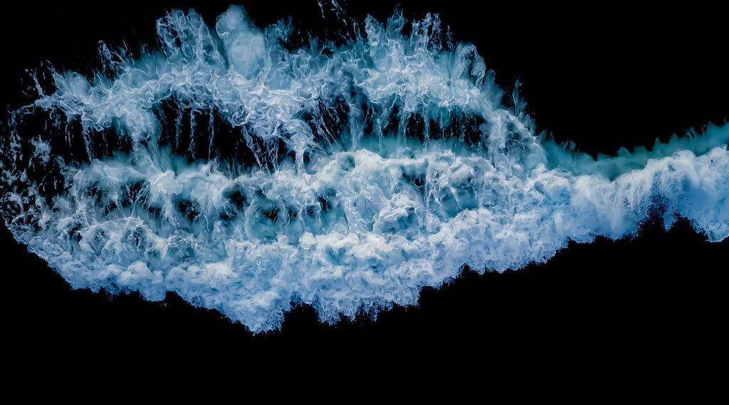 ARIEL SHOT OF WHITE WASH OF WAVES CRASHING OVER ROCKS.