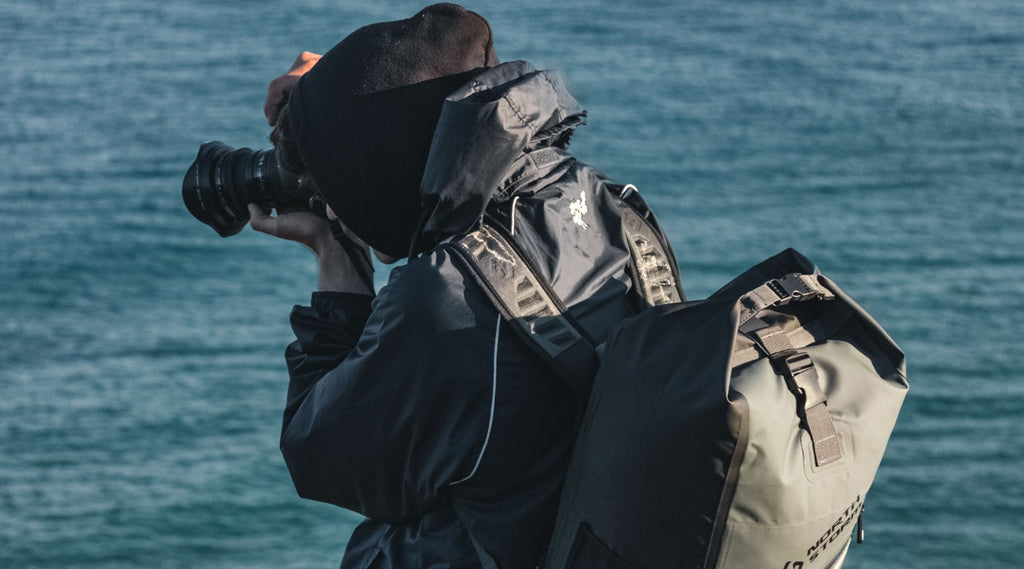 ETHAN TAKING A PHOTO HOLDING HIS CAMERA WEARING A NORTH STORM WATERPROOF BACKPACK.