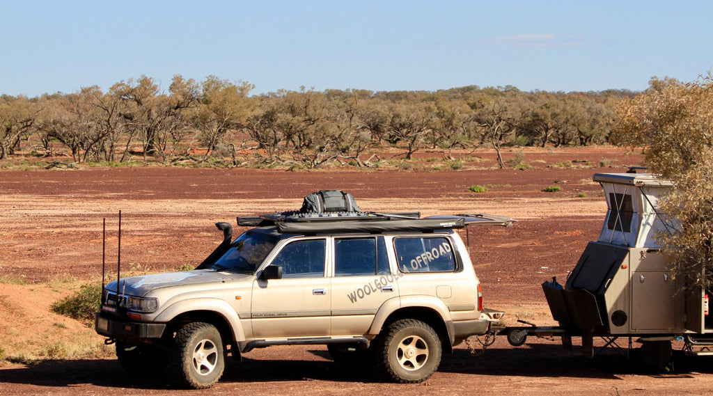 WOOLGOOLGA OFFROAD'S LANDCRUISER PARKED ON RED DIRT WITH A NORTH STORM WATERPROOF DUFFEL TIED TO THE ROOF RACKS.