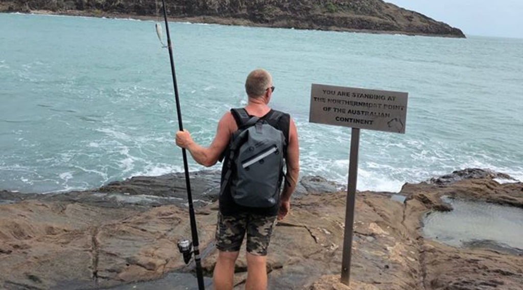 KEV OF WOOLGOOLGA OFFROAD STANDING AT THE MOST NORTHERN TIP OF AUSTRALIA HOLDING A FISHING ROD AND WEARING A NORTH STORM WATERPROOF BACKPACK.