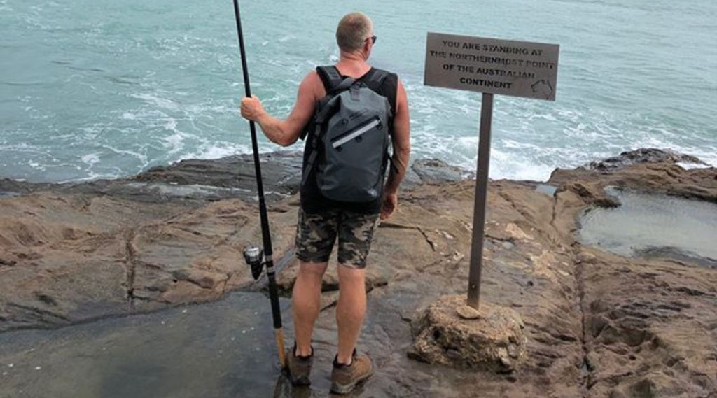 A man holding a fishing rod at the most Northern tip of Australia wearing a North Storm waterproof 30 litre backpack.