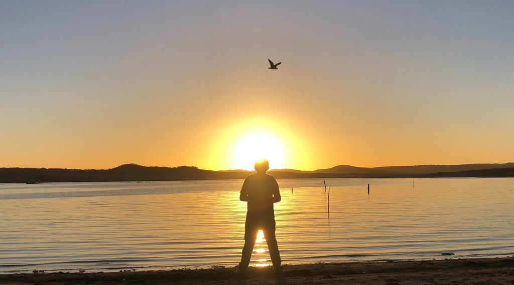 A MAN STANDING BY COPETON DAM WITH THE SUN SETTING.
