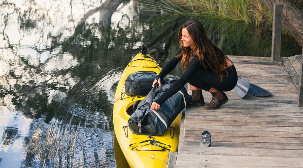 Girl placing a North Storm waterproof bag on a kayak smiling