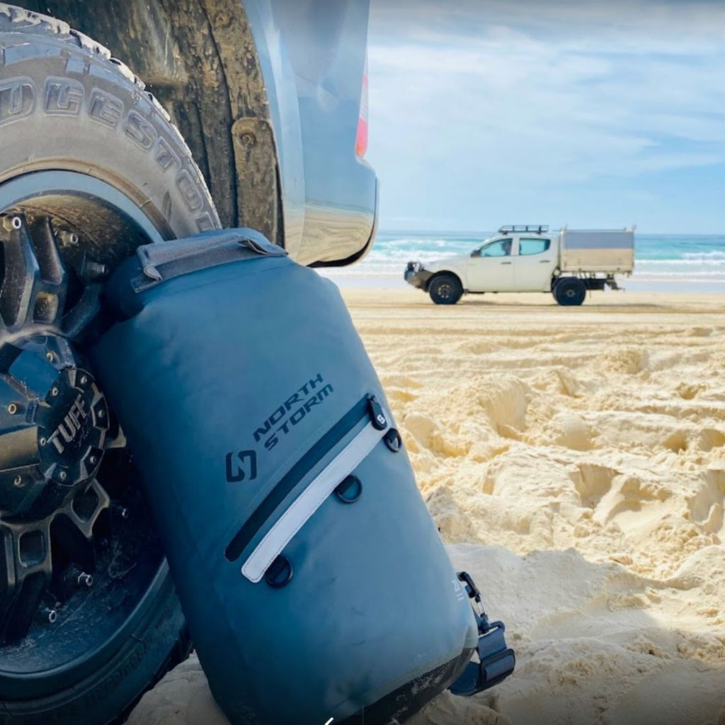 NORTH STORM DRY BAG LEANING AGAINST A CAR TYRE ON THE BEACH.