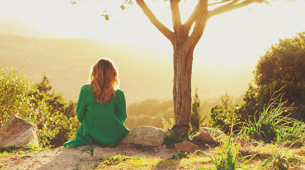 A LADY SITTING QUIETLY ALONE WITH NATURE SURROUNDING HER ON A SUNNY DAY.