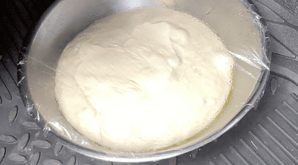 A BOWL OF BREAD DOUGH RISING IN A METAL BOWL ON THE FLOOR OF A CAR.