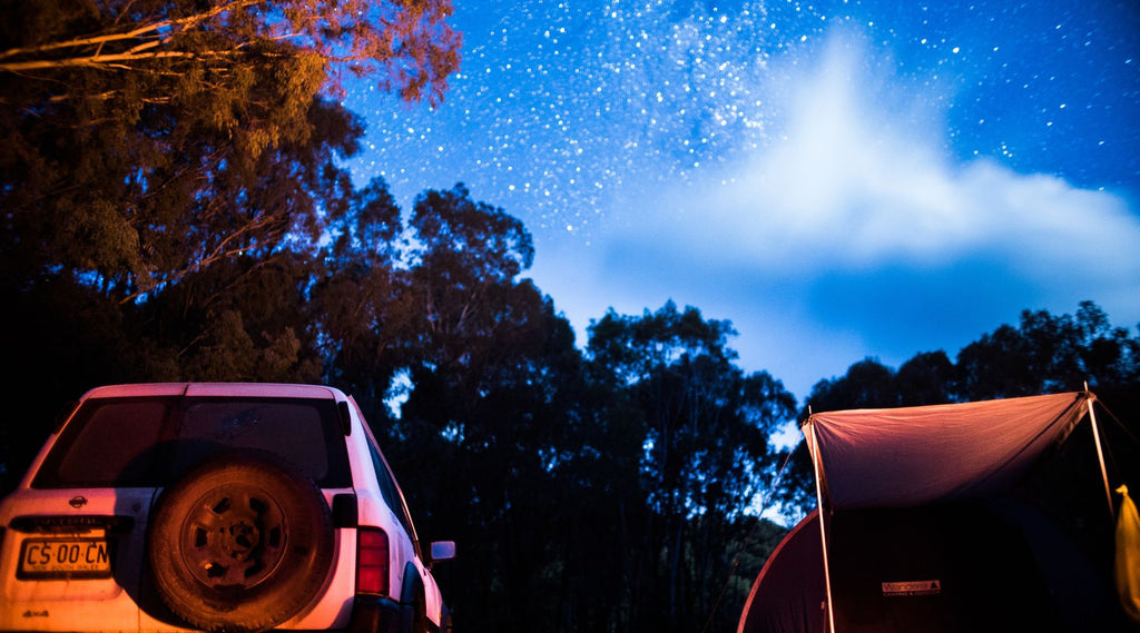 A tent and four wheel drive set up underneath a sky full of glittering stars.