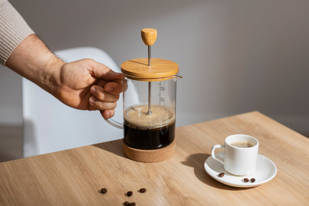 A steaming cup of coffee next to a French press and some whole coffee beans