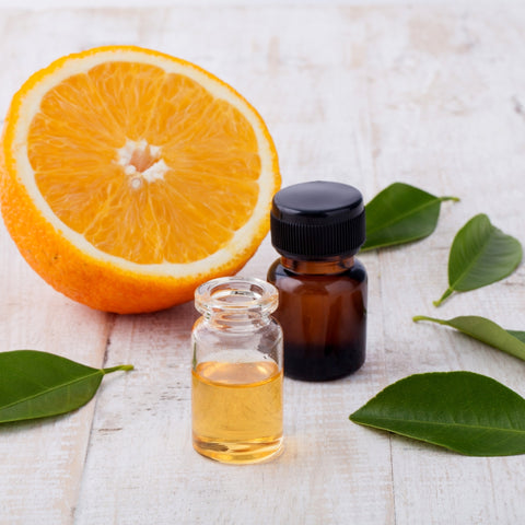 half of an orange behind 2 glass bottles filled half way with orange essential oil surrounded by 5 green leaves