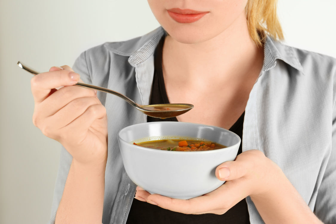Close-up of a person eating a small bowl of soup, symbolizing moderate consumption of a lentil-containing meal as part of a gout-friendly diet.