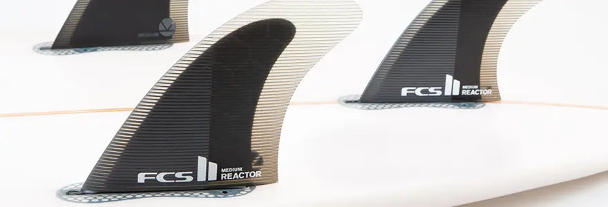 A close up of a set of FCS II Reactor Fins in a surfboard
