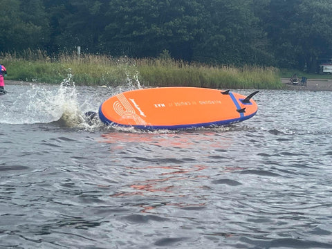 person in water having fallen off an orange paddleboard flipping over