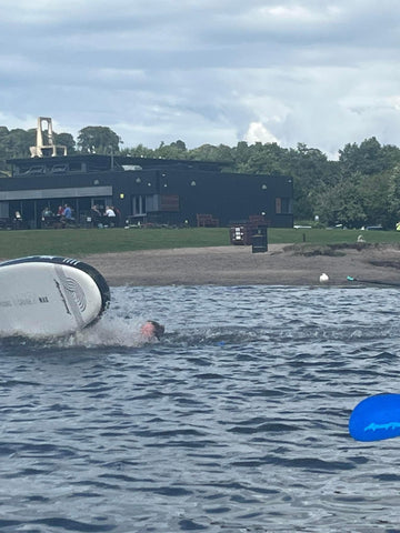 person swimming in water after falling off a white paddleboard