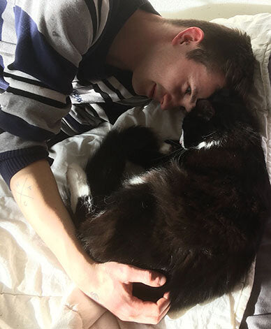 Del Boy the fluffy cat curls up with Anneli's partner, James. Their heads touch.