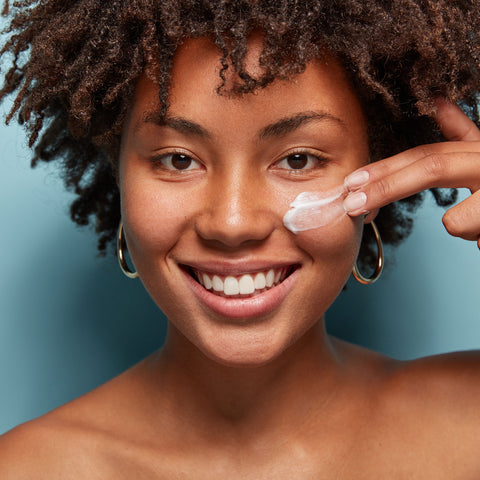 A woman of color applying sunscreen lotion to her cheek