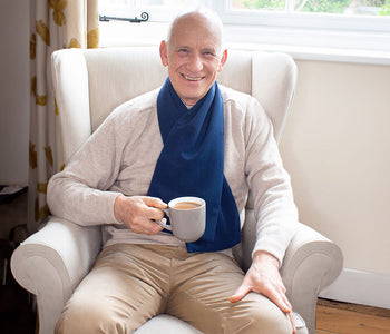 An older man drinking coffee on his living room couch while wearing the protective scarf bib.