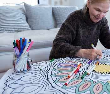 An older woman in her living room, coloring a bimoo mandala washable tablecloth.