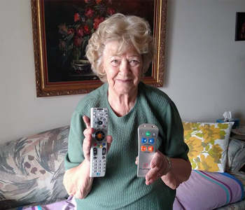 An older woman holding a conventional TV remote in one hand, and the simplified 5 button Flipper remote in the other.