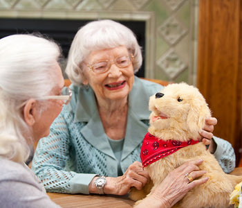 Two elderly women with the Joy for All golden lifelike pup designed for people living with dementia.