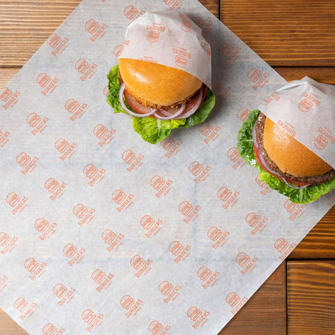 Custom deli paper featuring logo-printed design, wrapping two delicious burgers on a rustic wooden table.